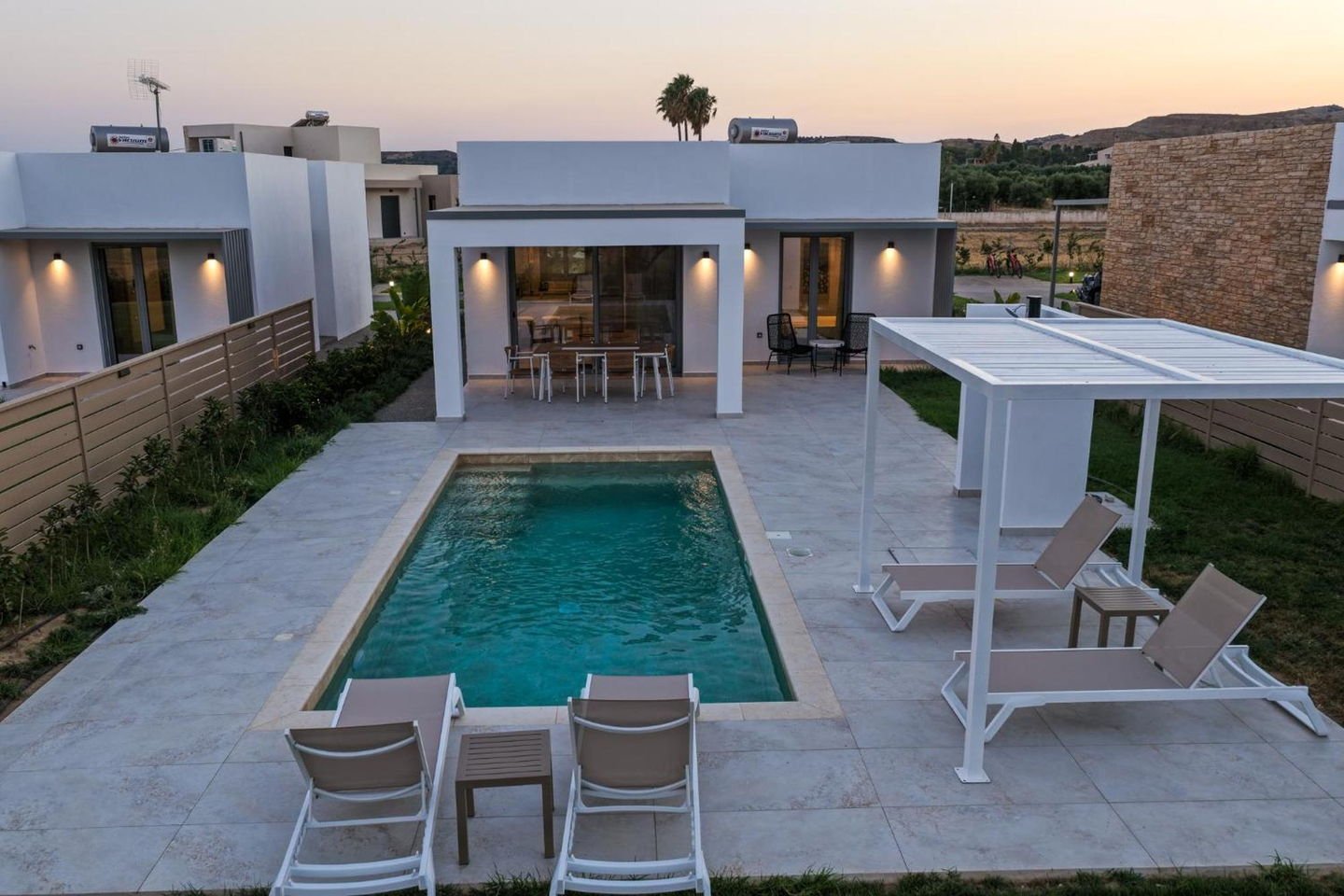 Private pool and shaded pergola lit at dusk at ŌNAR Villas